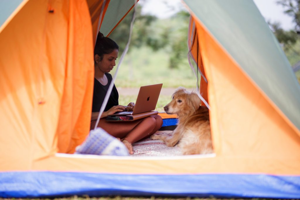 A woman sitting in her tent with her dog and a laptop trying to get WiFi at a campground