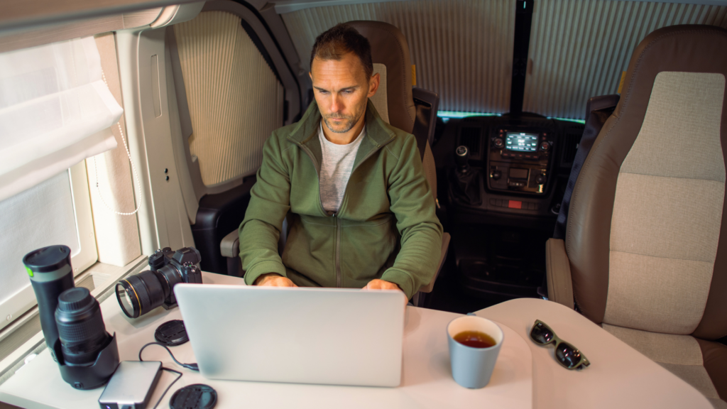 A man sitting inside his RV with his laptop open and camera equipment all around 