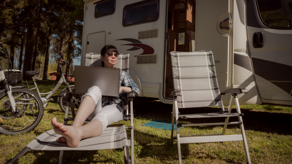 A woman sitting in a chair outside of her RV with her laptop smiling. Campground internet is one of the best way to get WiFi in an RV